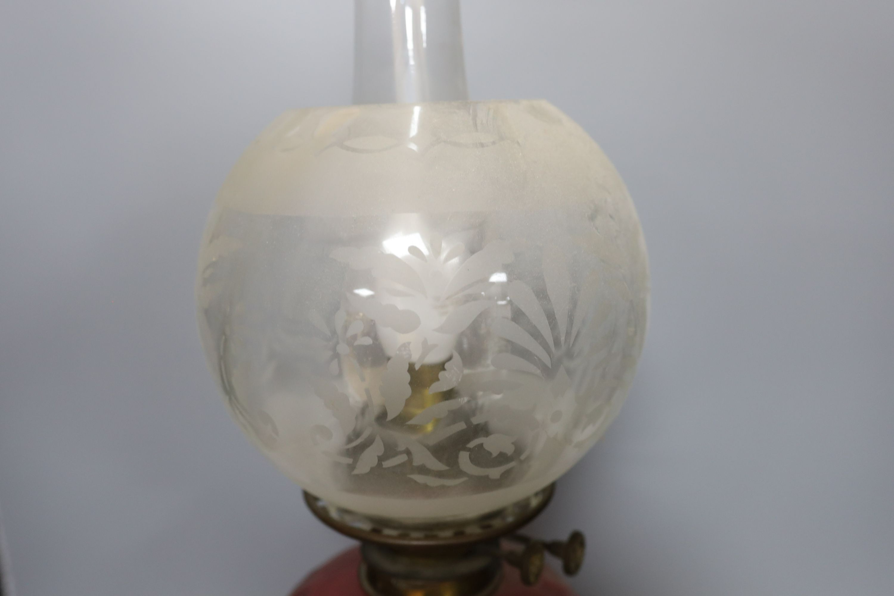 An Edwardian oil lamp with ruby glass font, later inverted to electricity, 57 cms high including funnel.